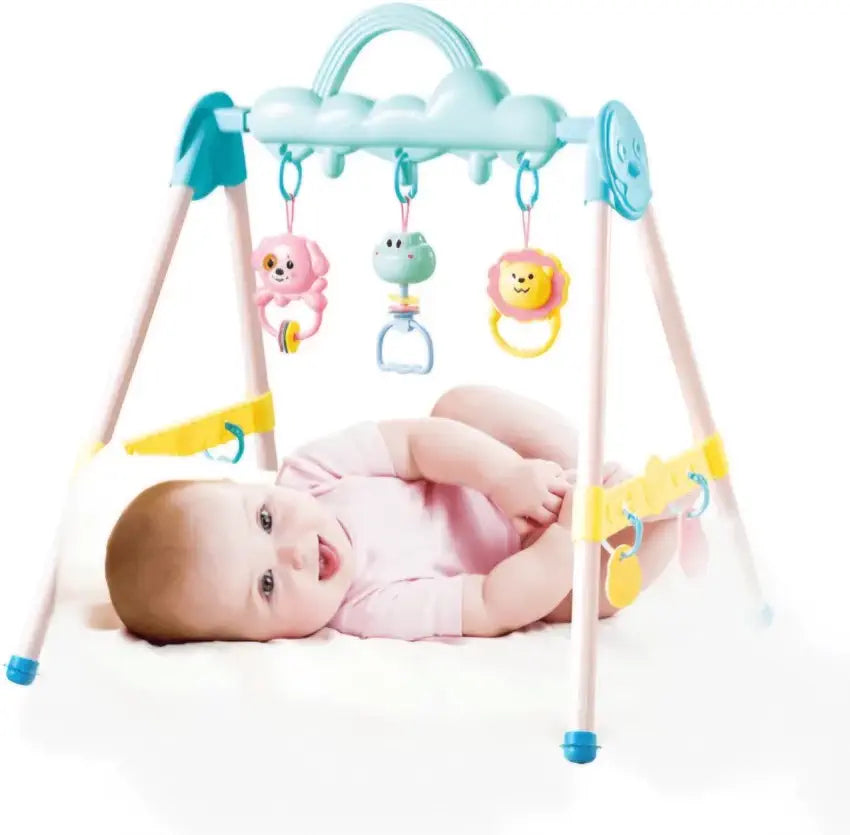 Baby lying on a white blanket next to a colorful baby gym with hanging toys.