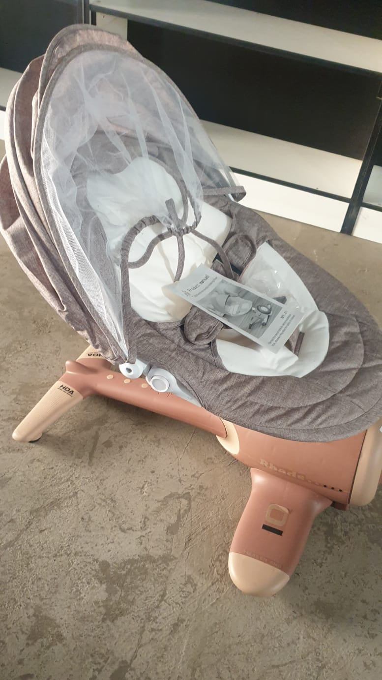 Baby swing chair with canopy on a white rug in a room with striped wallpaper